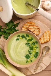 Photo of Delicious leek soup served on beige wooden table, flat lay