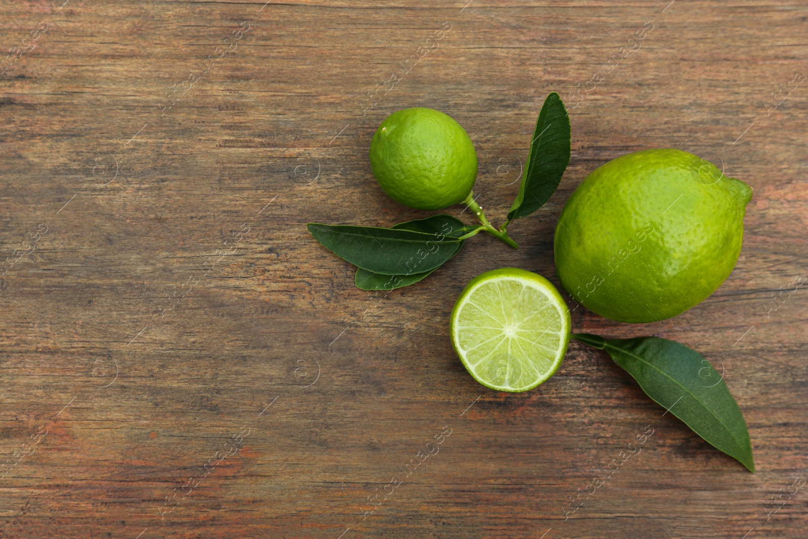 Photo of Whole and cut fresh ripe limes with green leaves on wooden table, flat lay. Space for text