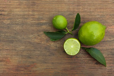 Whole and cut fresh ripe limes with green leaves on wooden table, flat lay. Space for text