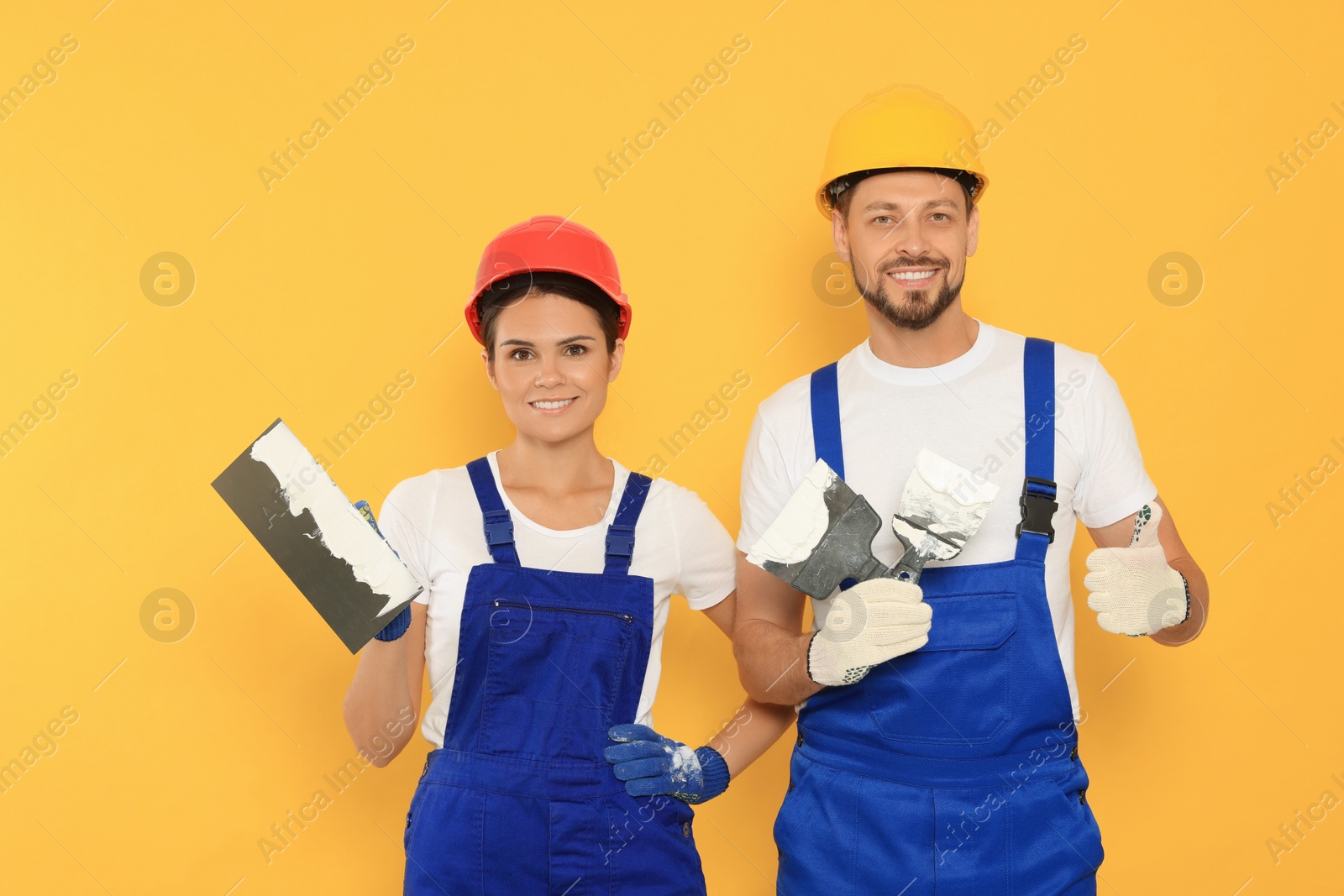 Photo of Professional workers with putty knives in hard hats on orange background