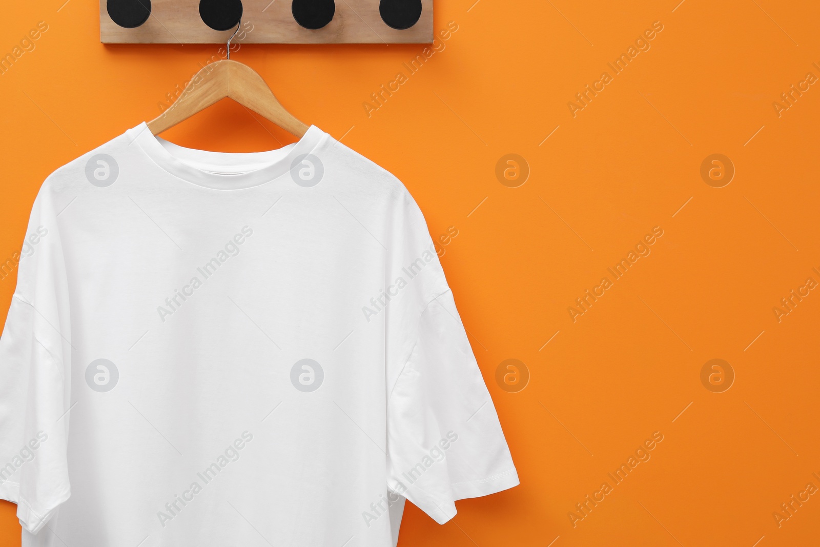 Photo of Hanger with white T-shirt on orange wall, space for text