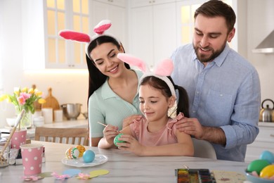 Photo of Happy family painting Easter eggs at table in kitchen