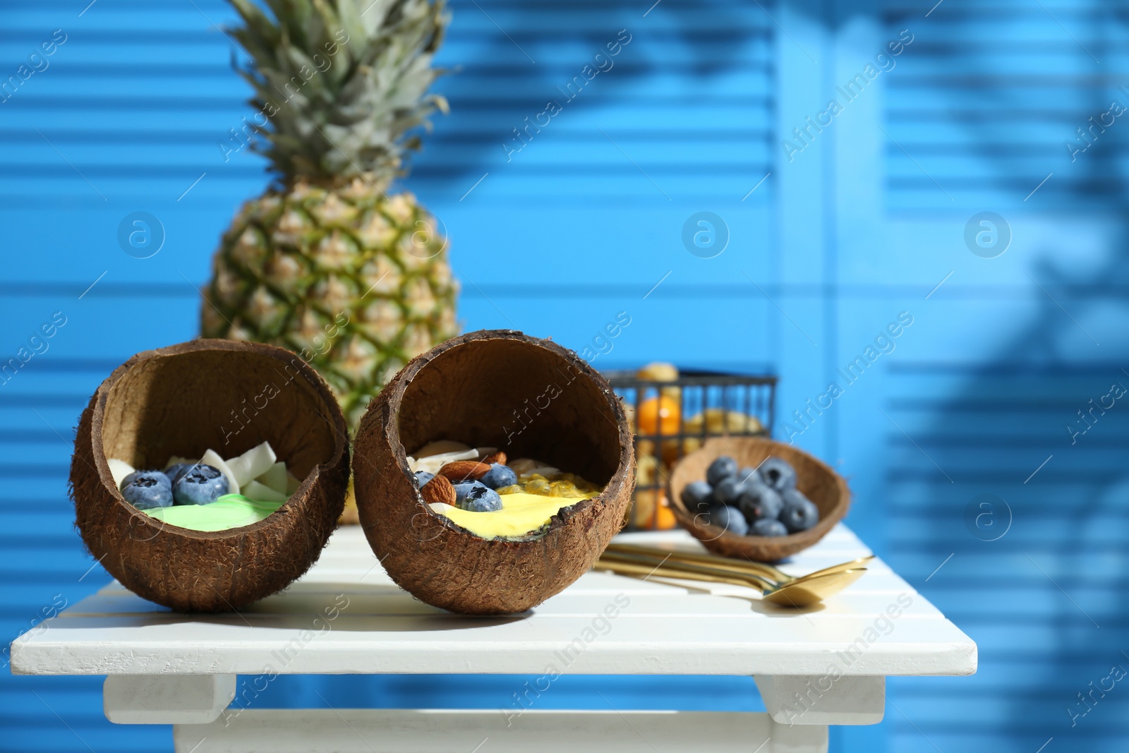 Photo of Tasty smoothie bowl served in coconut shells on white wooden table