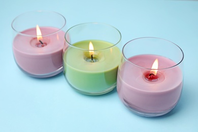 Burning wax candles in glass holders on light blue background