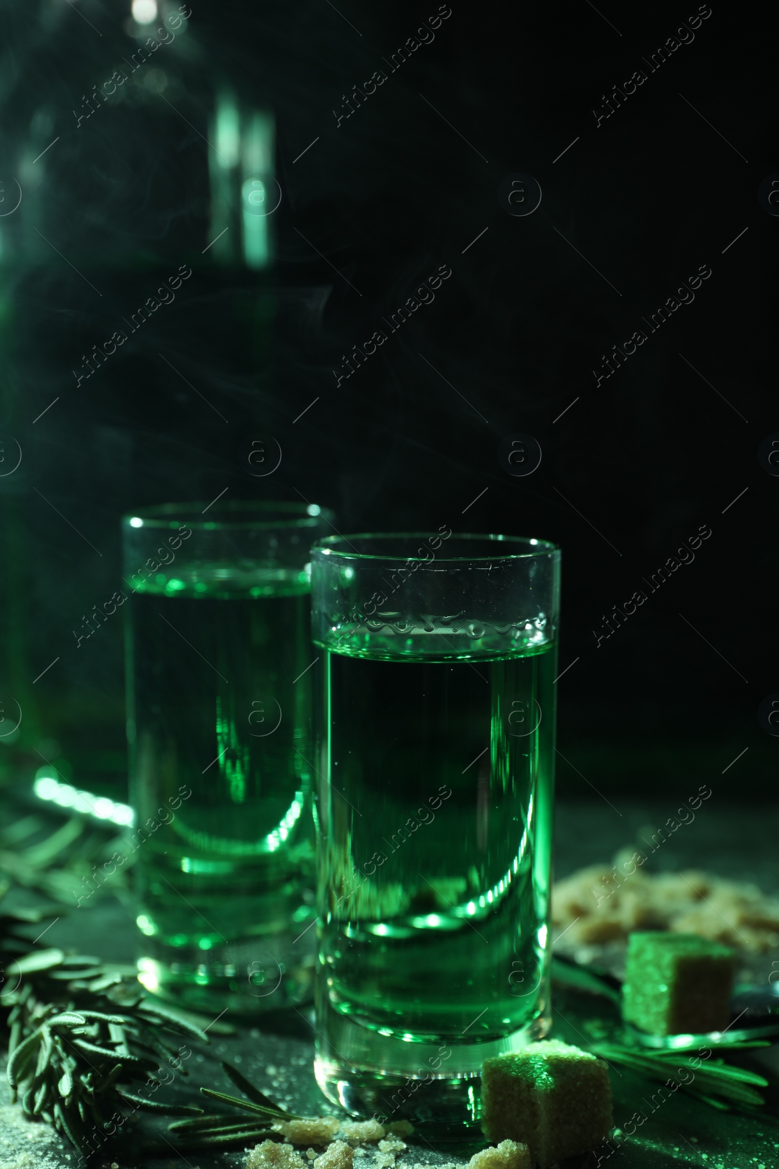 Photo of Absinthe in shot glasses, rosemary and brown sugar on table, closeup. Alcoholic drink