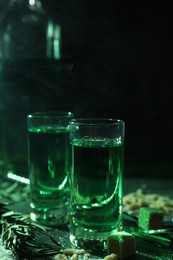 Photo of Absinthe in shot glasses, rosemary and brown sugar on table, closeup. Alcoholic drink