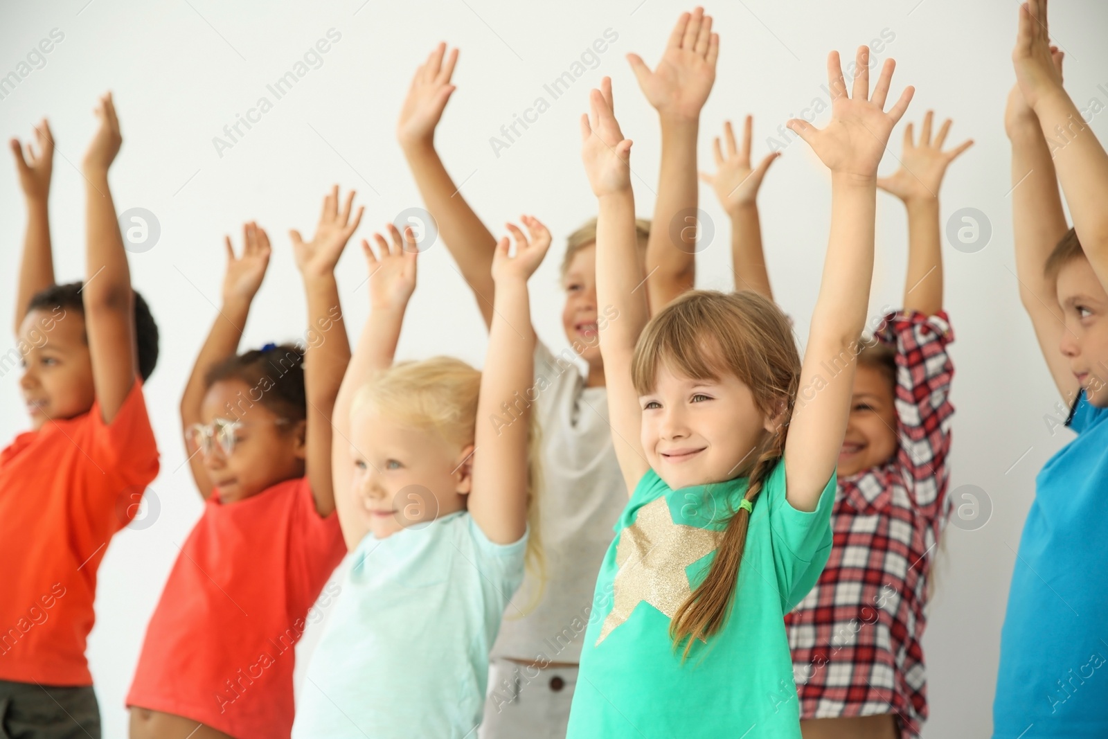 Photo of Little children raising hands together on light background. Unity concept