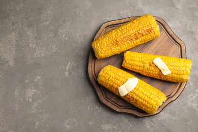 Delicious grilled corn with butter on grey table, top view. Space for text