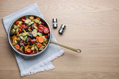 Photo of Frying pan with tasty cooked vegetables and mushrooms on wooden table, flat lay. Space for text