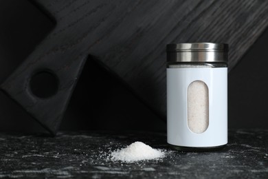 Stylish shaker with salt on dark table. Space for text