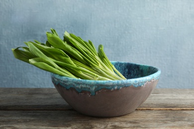 Photo of Bowl with wild garlic or ramson on wooden table against color background