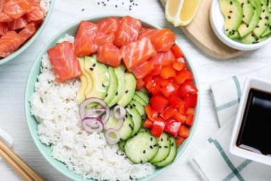 Delicious poke bowl with salmon and vegetables served on white wooden table, flat lay