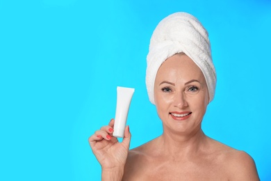 Portrait of beautiful mature woman with perfect skin holding tube of cream on light blue background