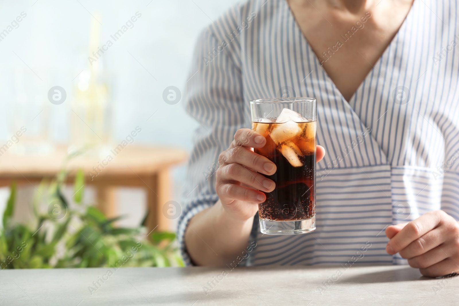 Photo of Woman with glass of cold cola at table indoors, closeup. Space for text