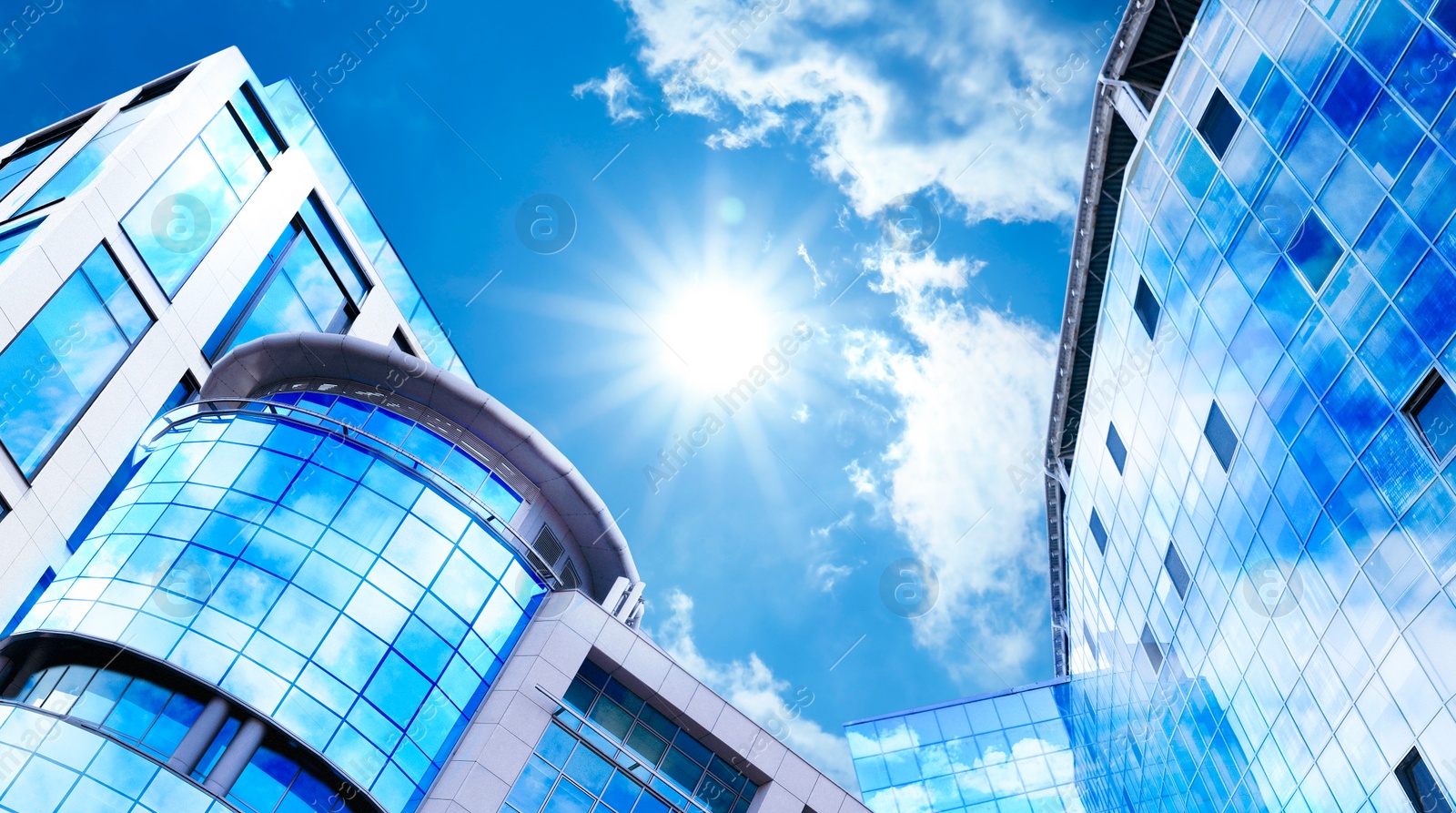 Image of Beautiful blue sky with clouds reflecting in windows. Low angle view of modern buildings on sunny day