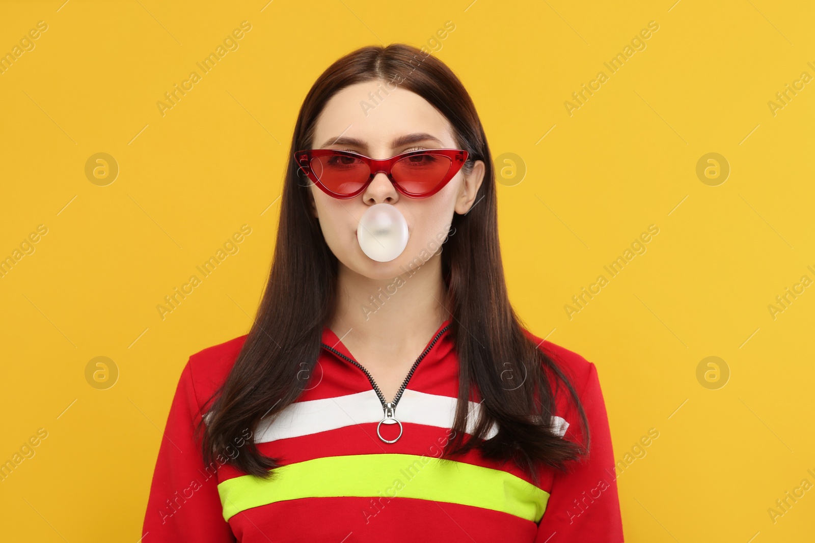 Photo of Beautiful woman in sunglasses blowing bubble gum on orange background