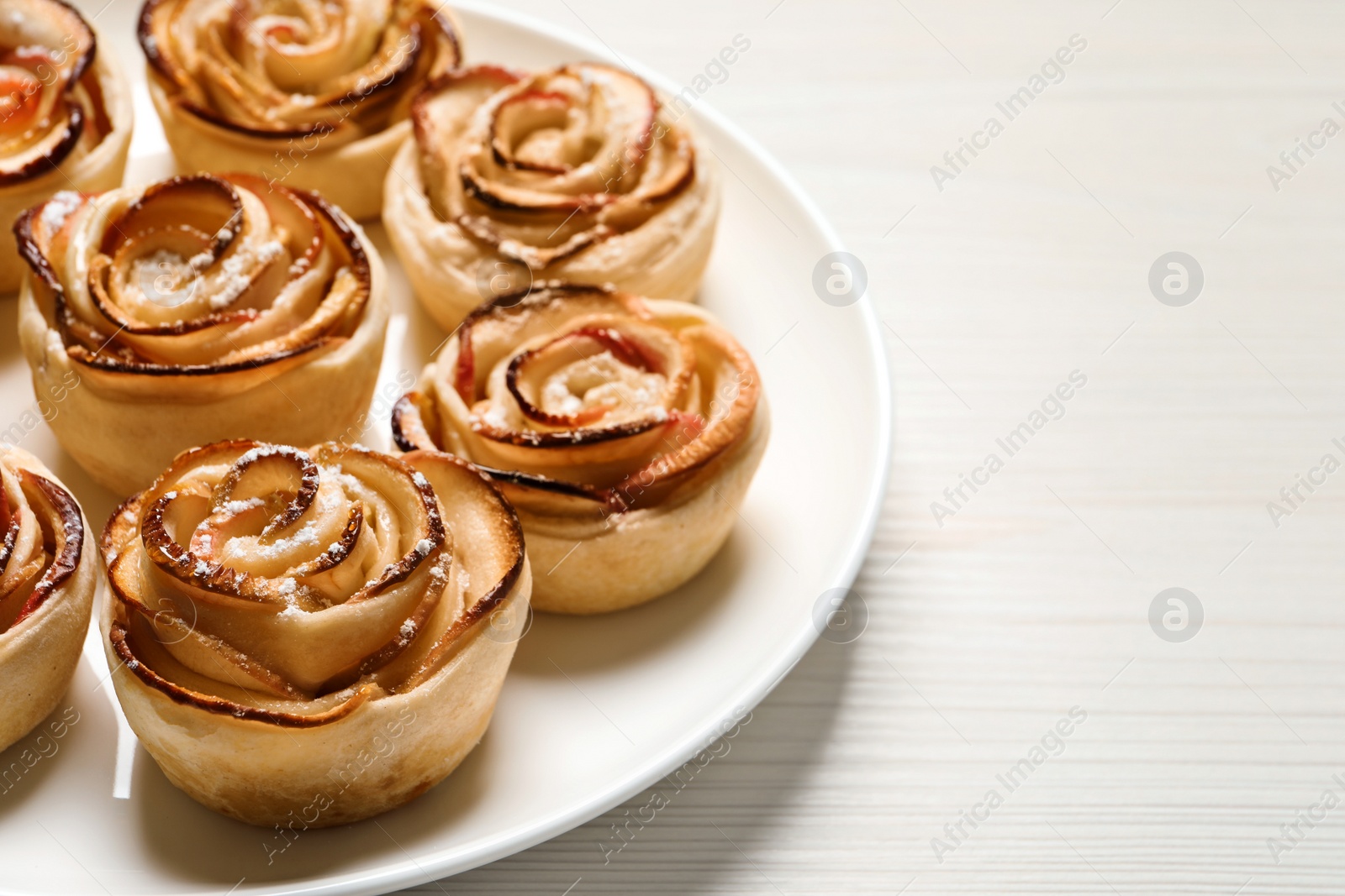 Photo of Freshly baked apple roses on white wooden table, space for text. Beautiful dessert