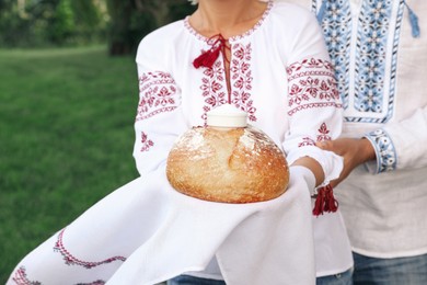 Mature couple in national clothes with bread and salt outdoors, closeup. Ukrainian welcoming tradition