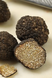Photo of Whole and cut black truffles on light table, closeup