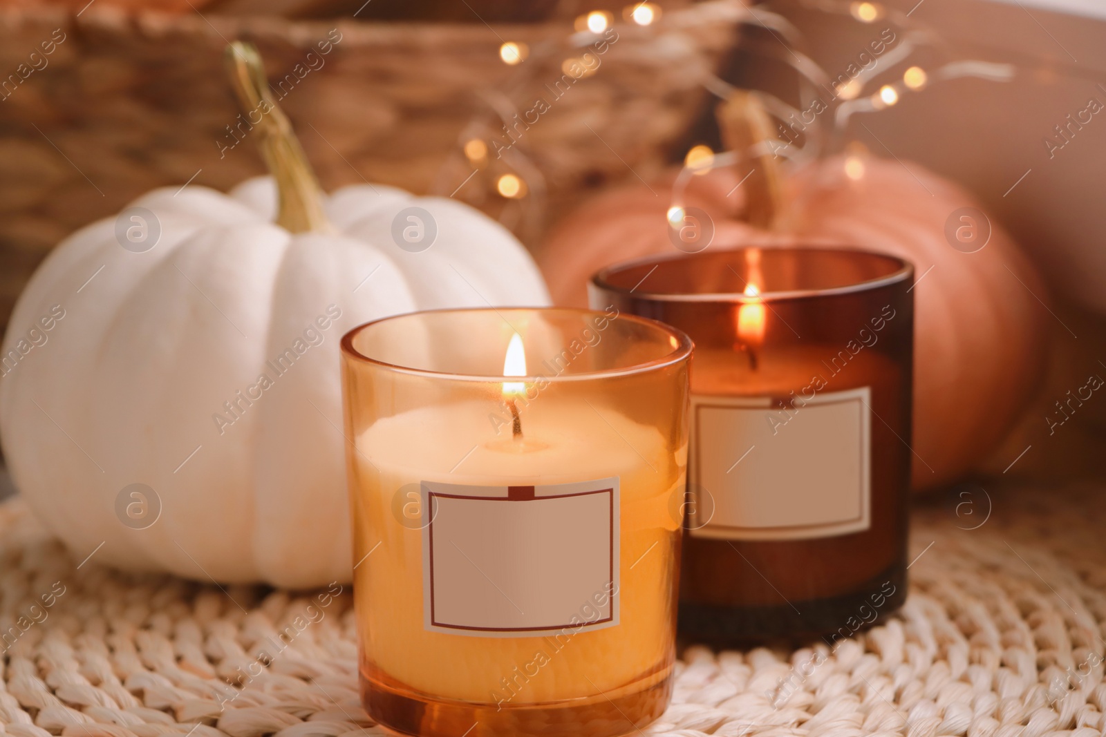 Photo of Scented candles and pumpkins on wicker mat indoors, closeup