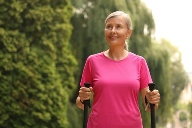 Photo of Senior woman with Nordic walking poles outdoors, space for text