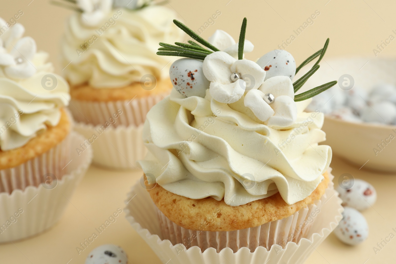 Photo of Tasty Easter cupcakes with vanilla cream and candies on beige background, closeup