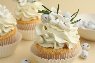 Photo of Tasty Easter cupcakes with vanilla cream and candies on beige background, closeup