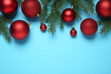 Photo of Red Christmas balls and fir tree branches on light blue background, flat lay. Space for text