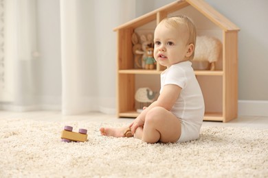 Children toys. Cute little boy playing with wooden car on rug at home, space for text