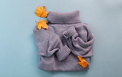 Warm sweater and dry leaves on light blue background, flat lay. Autumn season