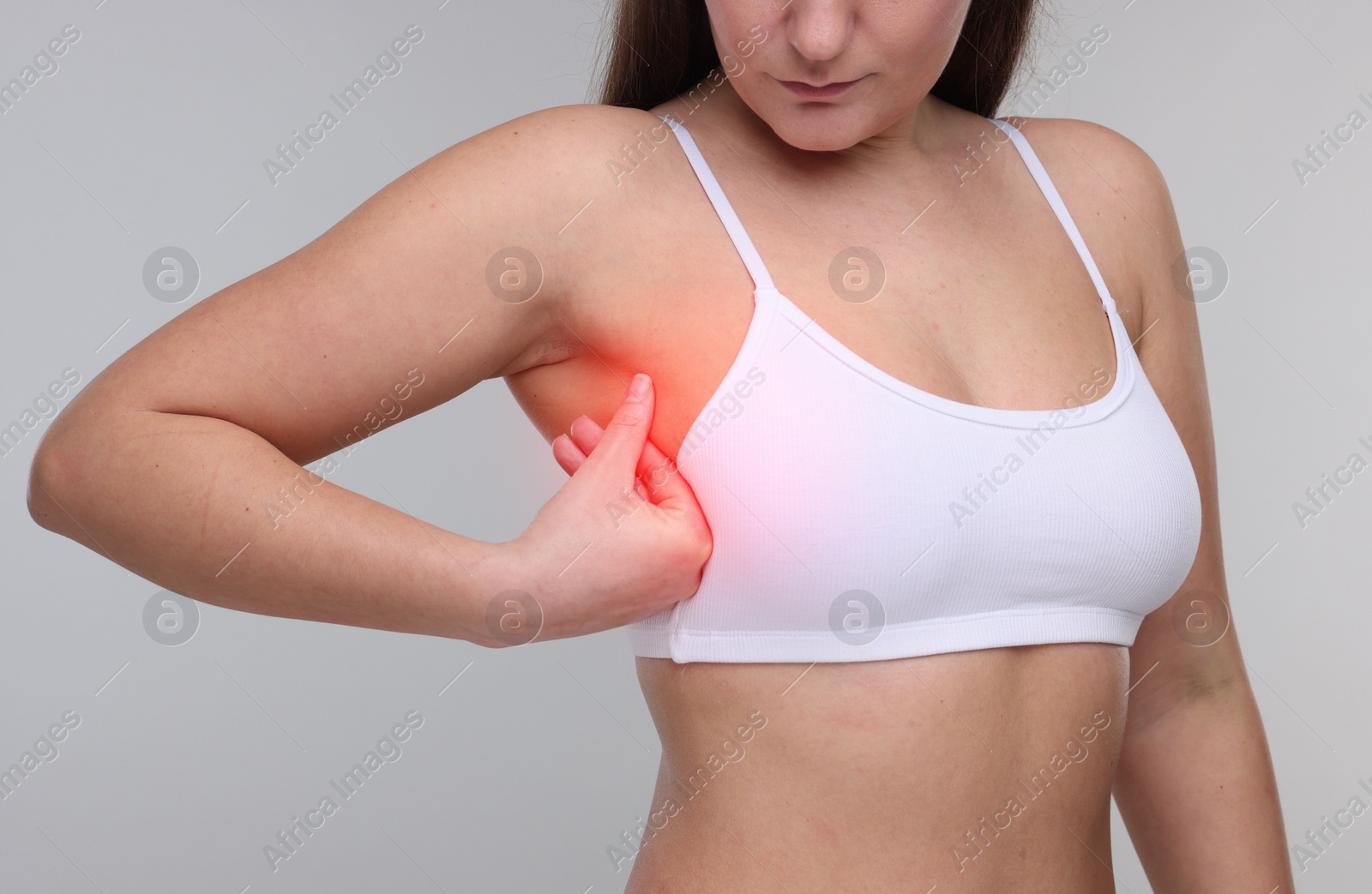 Image of Young woman suffering from breast pain on light grey background, closeup