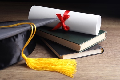 Graduation hat, books and student's diploma on wooden table