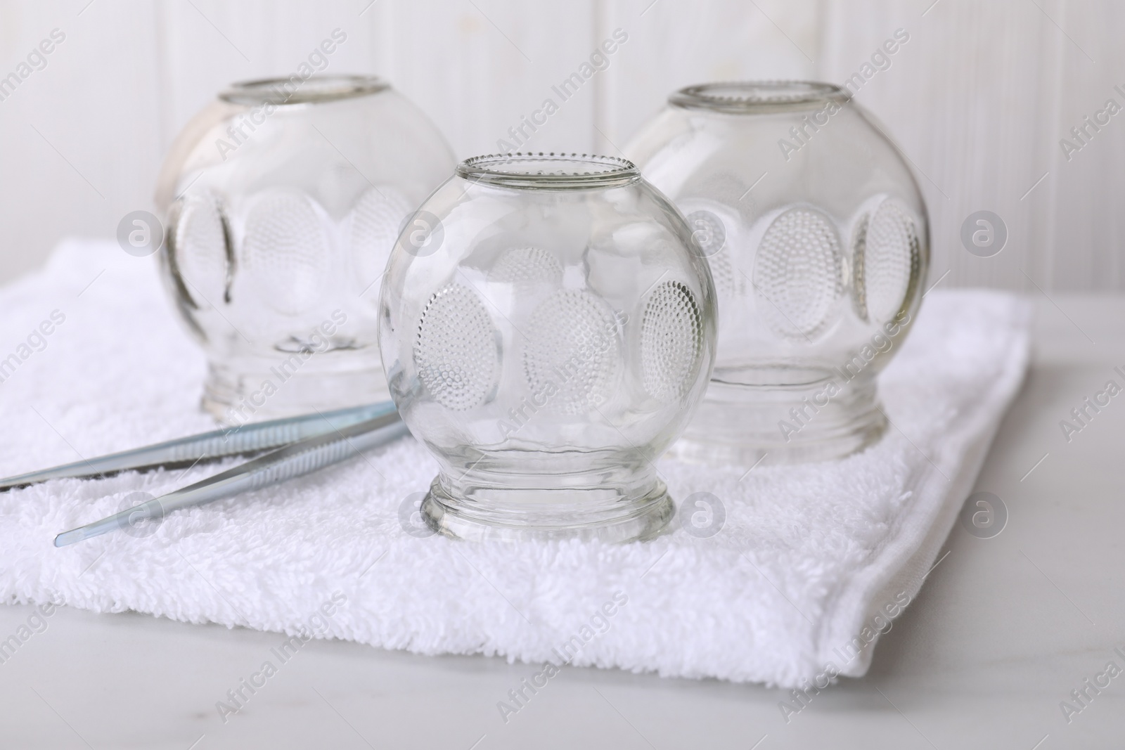 Photo of Glass cups and tweezers on white table, closeup. Cupping therapy