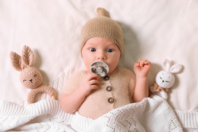 Photo of Cute newborn baby with pacifier and toys on white knitted plaid, top view