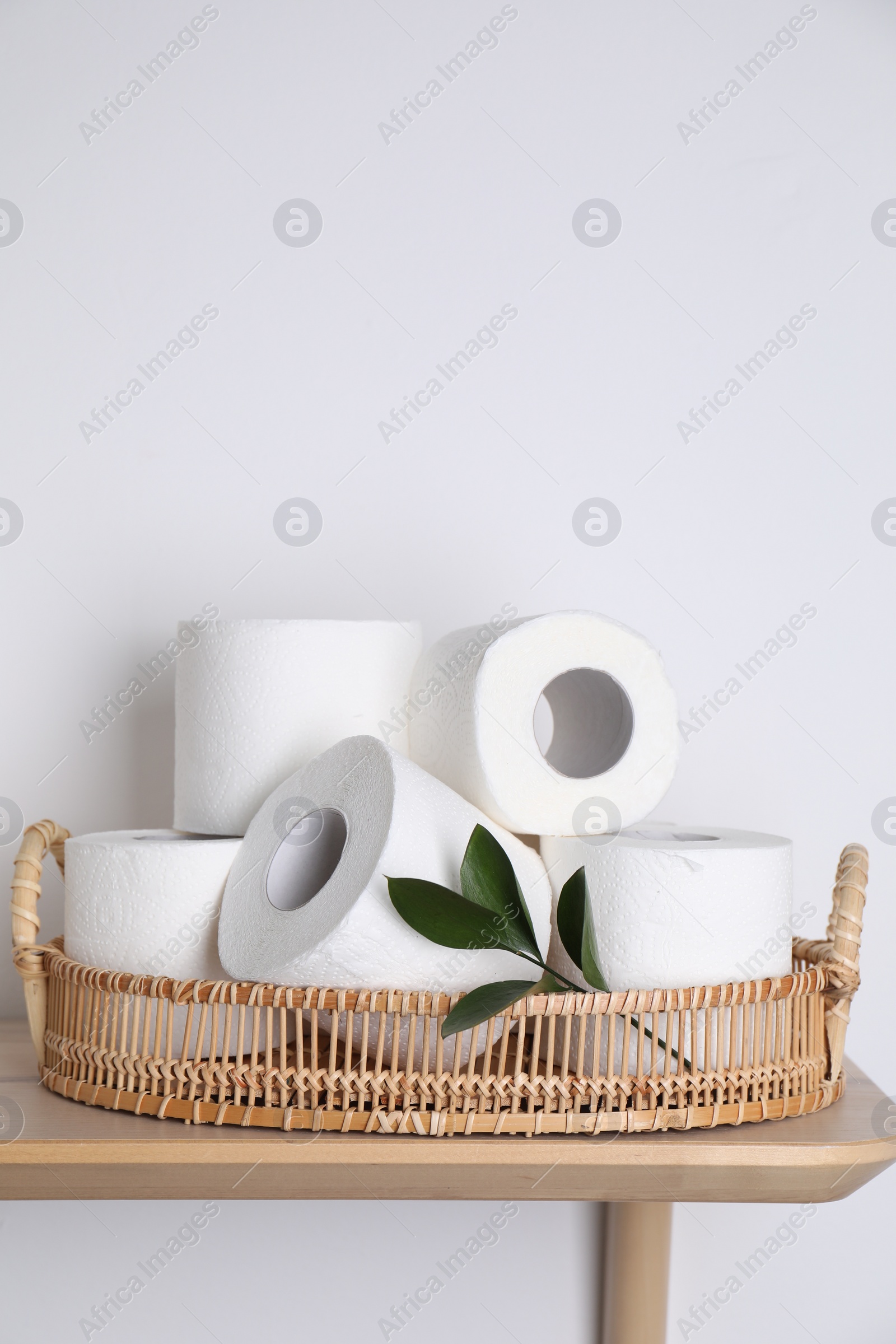 Photo of Toilet paper rolls and green leaves on wooden table near white wall