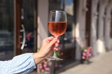 Woman holding glass of rose wine outdoors, closeup