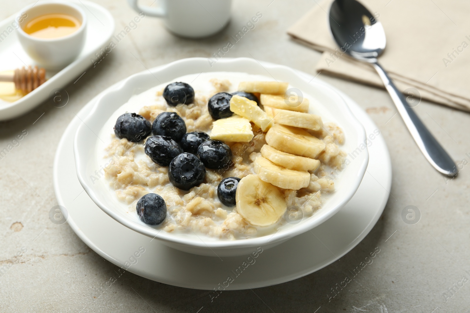 Photo of Tasty oatmeal with banana, blueberries, butter and milk served in bowl on light grey table