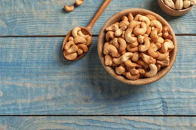 Photo of Tasty cashew nuts in bowl and spoon on color wooden table, flat lay. Space for text