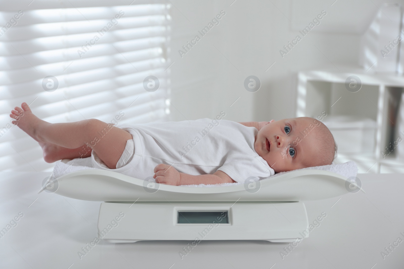 Photo of Cute little baby lying on scales in clinic