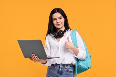 Student with laptop showing thumb up on yellow background