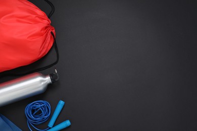 Photo of Red drawstring bag, skipping rope and thermo bottle on black background, flat lay. Space for text