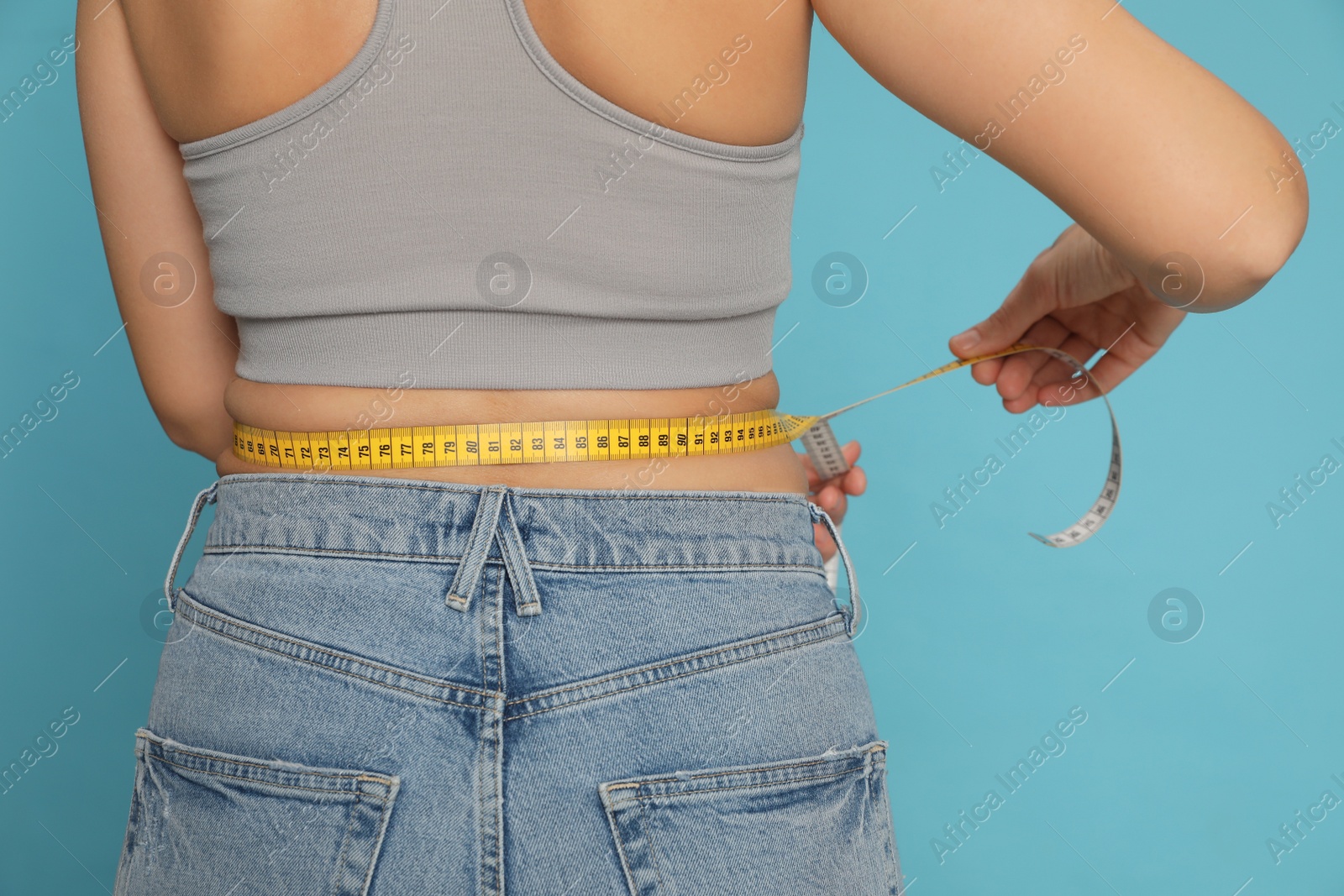 Photo of Woman measuring waist with tape on turquoise background, closeup