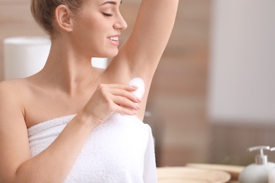 Beautiful young woman applying deodorant after shower in bathroom. Space for text