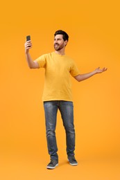 Photo of Smiling man taking selfie with smartphone on yellow background