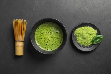 Photo of Cup of fresh matcha tea, bamboo whisk and green powder on black table, flat lay