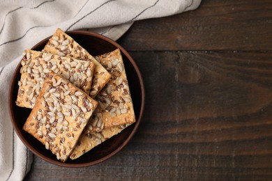 Photo of Cereal crackers with flax, sunflower and sesame seeds in bowl on wooden table, top view. Space for text