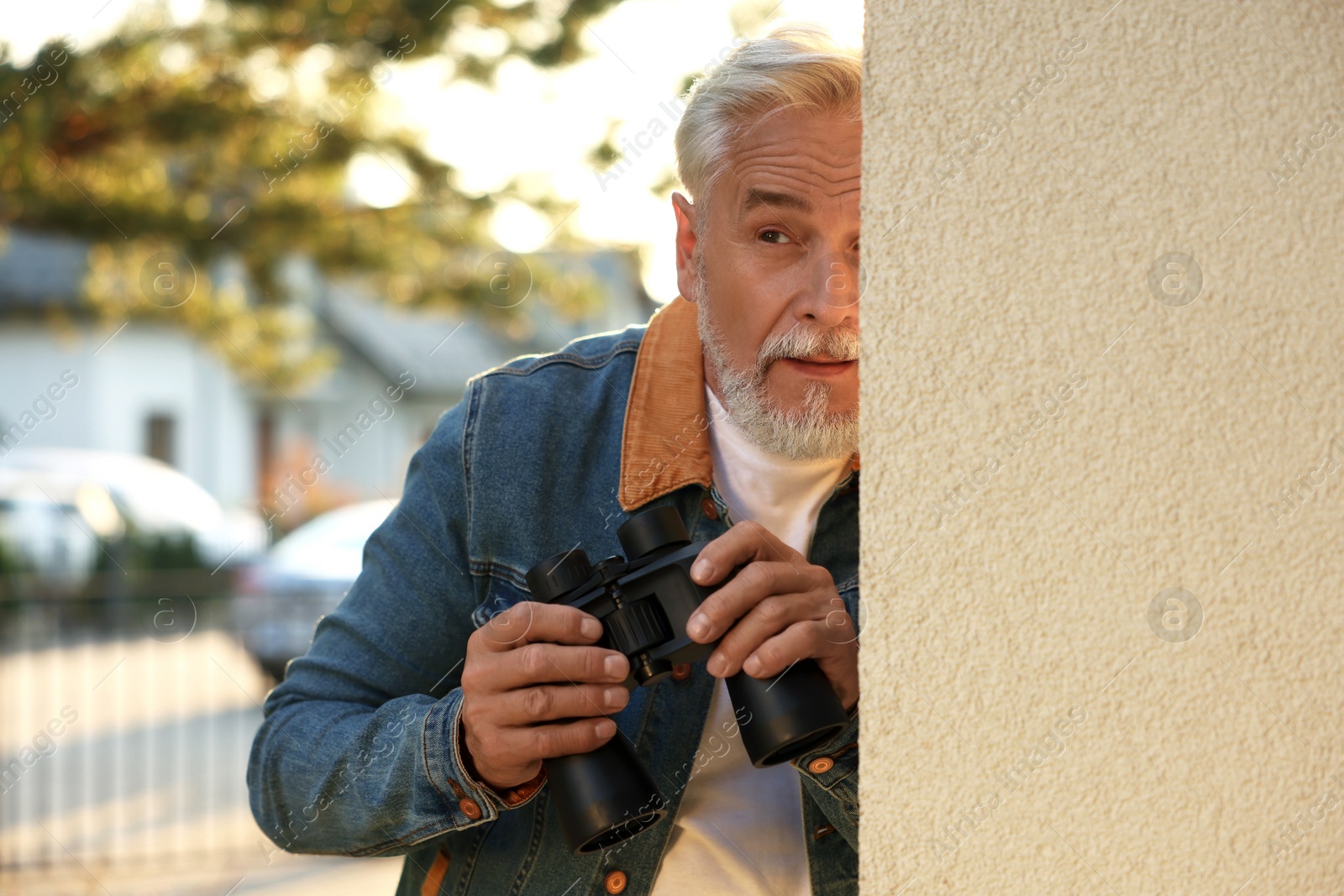 Photo of Concept of private life. Curious senior man with binoculars spying on neighbours outdoors