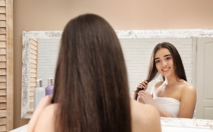 Beautiful young woman with hair comb near mirror in bathroom