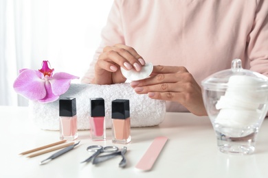 Woman removing polish from nails with cotton pad at table, closeup