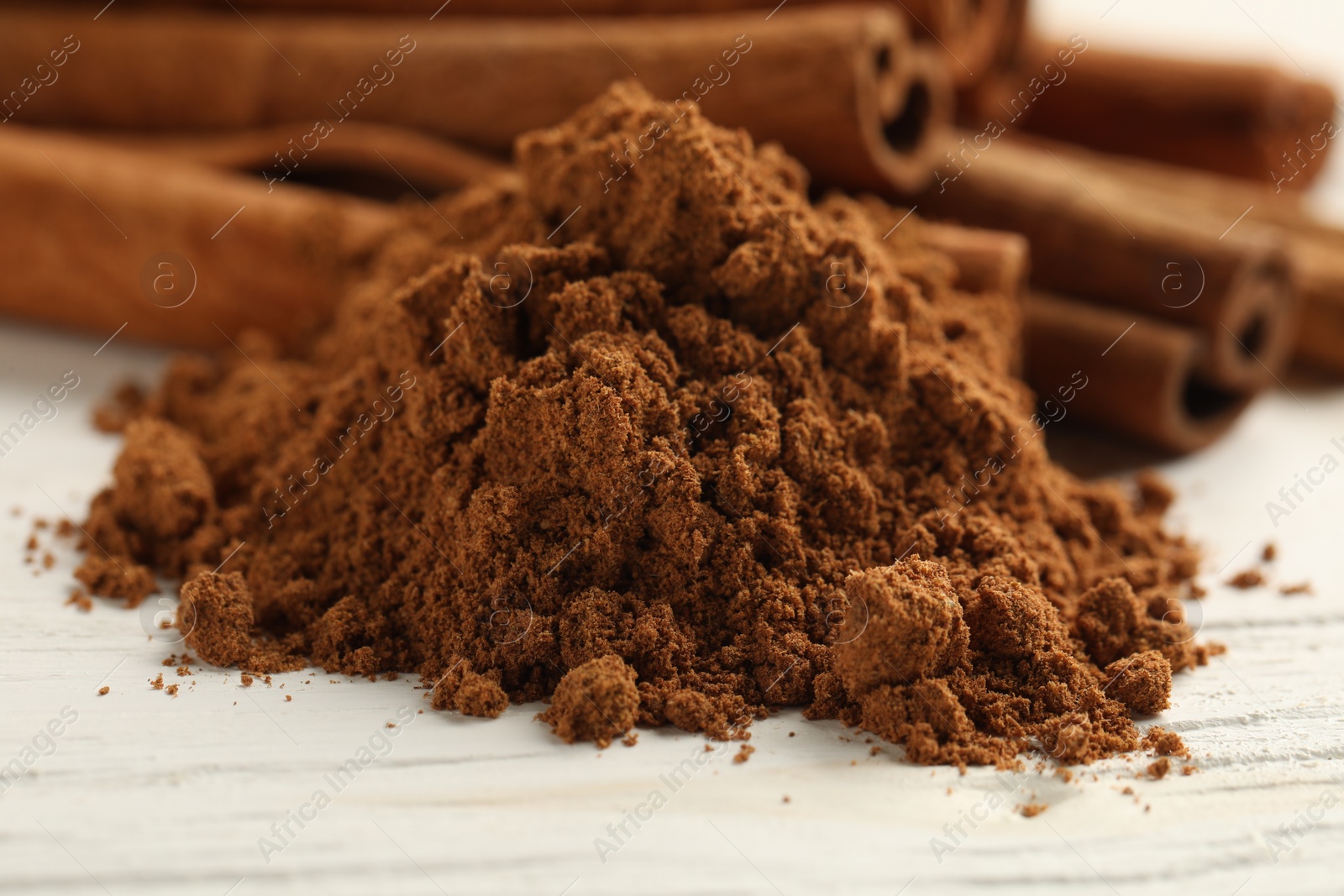 Photo of Aromatic cinnamon powder and sticks on white wooden table, closeup